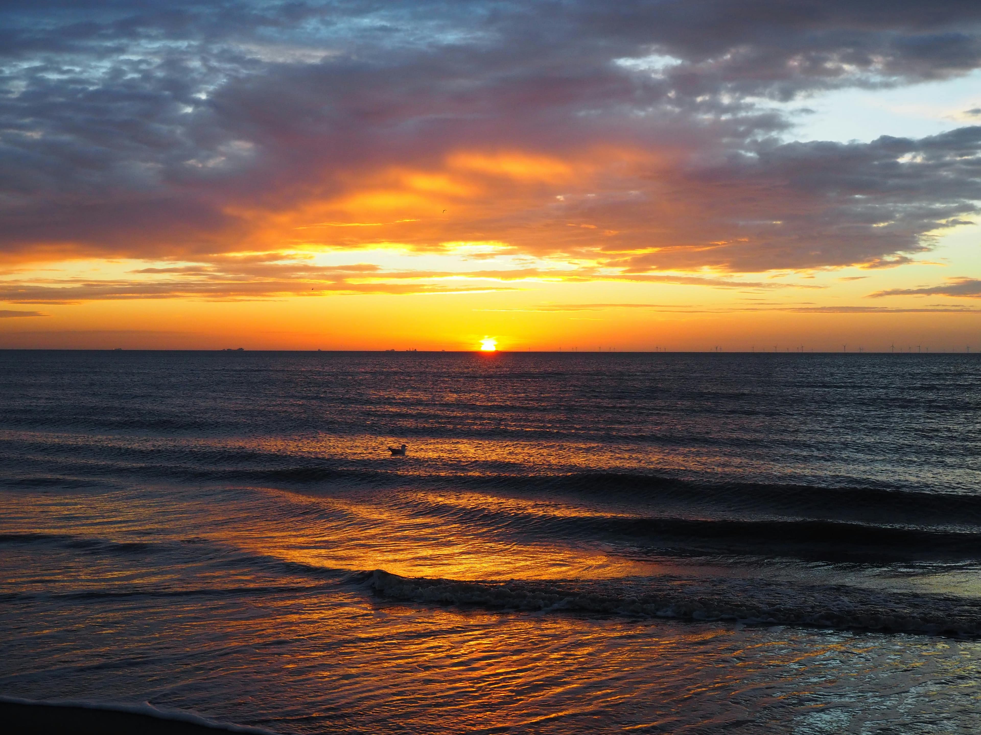 Orange sunset over the sea beneath dark clouds, with small waves reflecting the light.