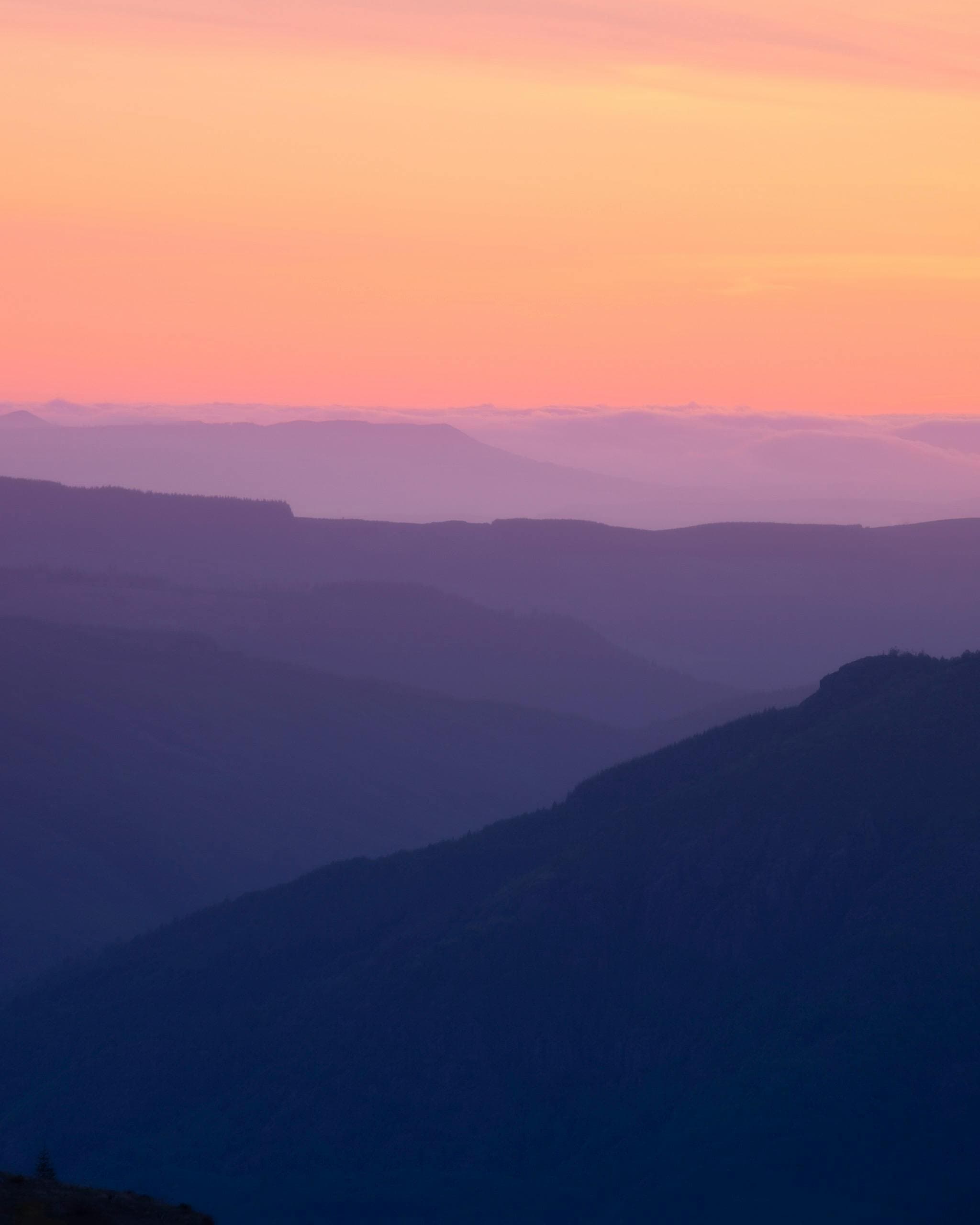Layered mountain ridges beneath a pink and orange sky at sunrise.