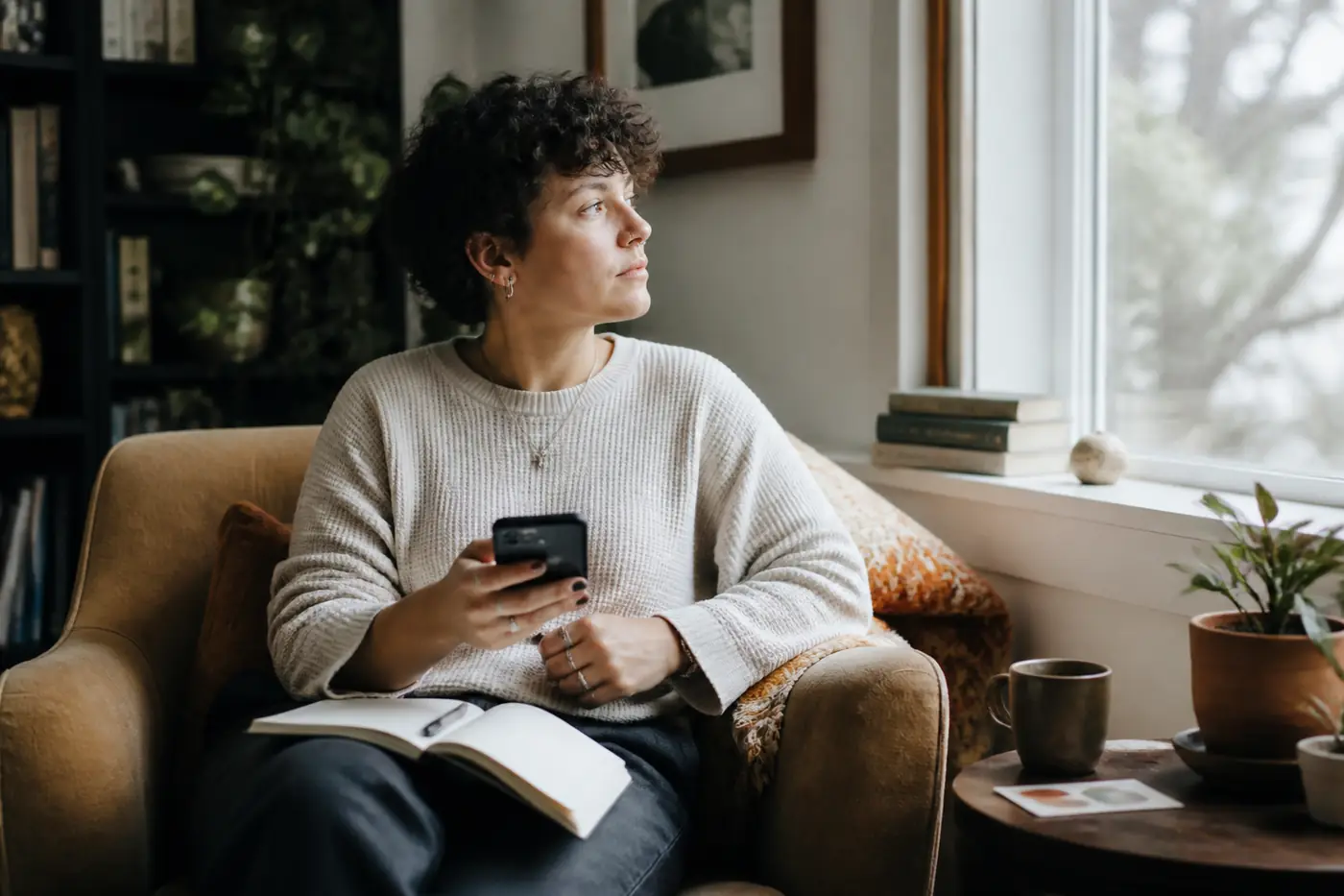 A person reflecting with a journal and phone beside a bright window