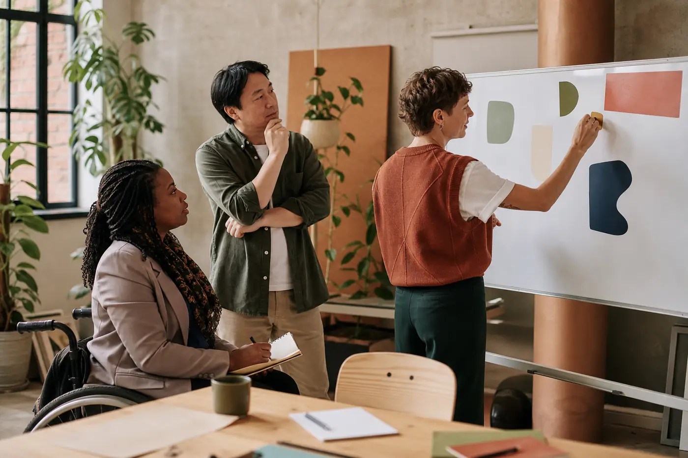 Three coworkers discussing abstract shapes on a studio whiteboard