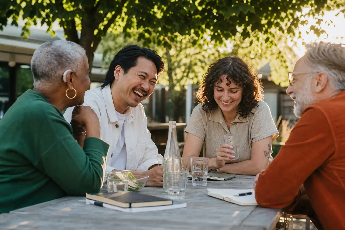 Four coworkers laughing together at an outdoor lunch table