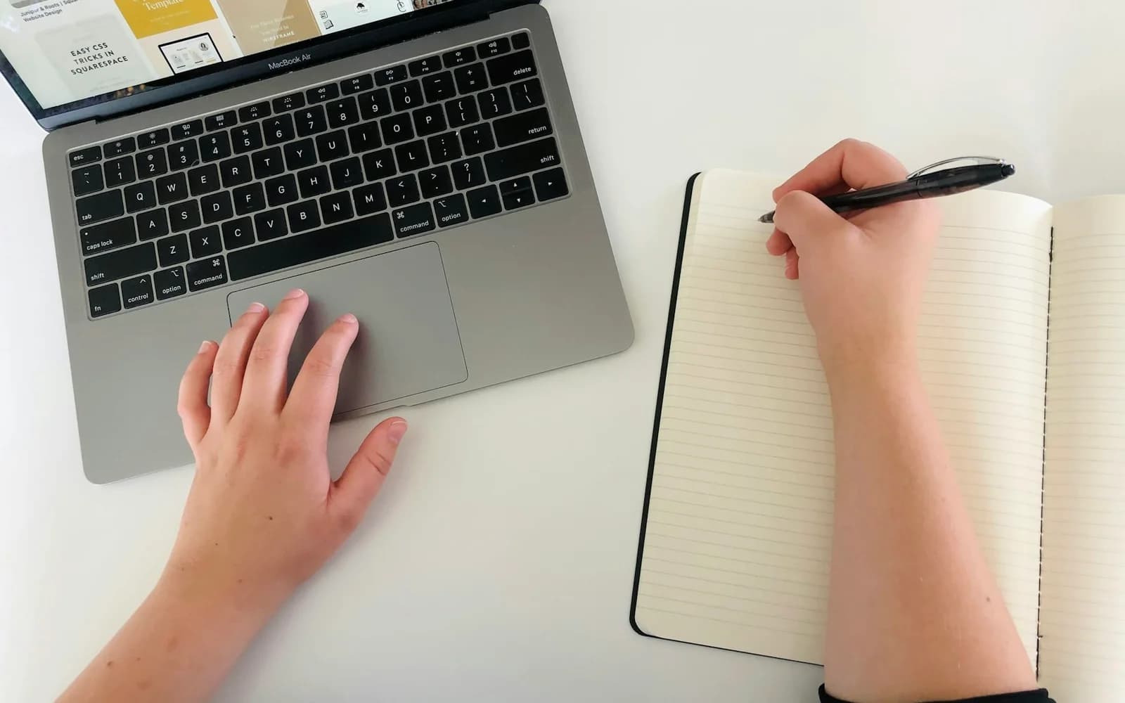 A person writes in a notebook while using a laptop.