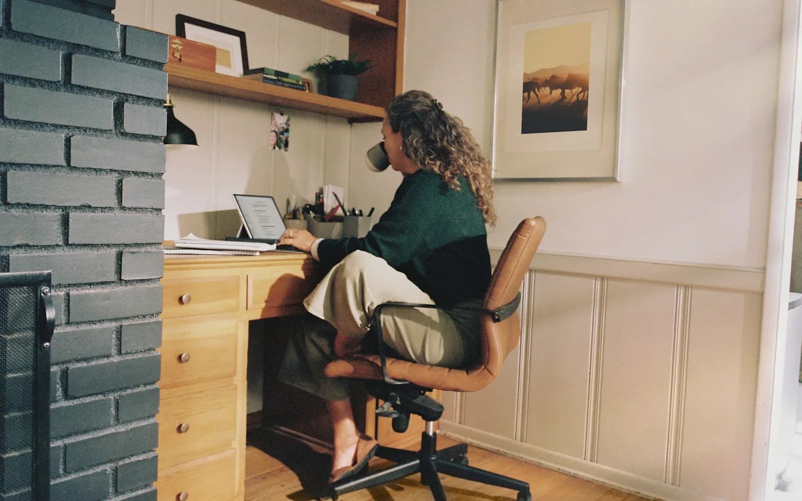 A woman works at a compact home desk with coffee nearby.