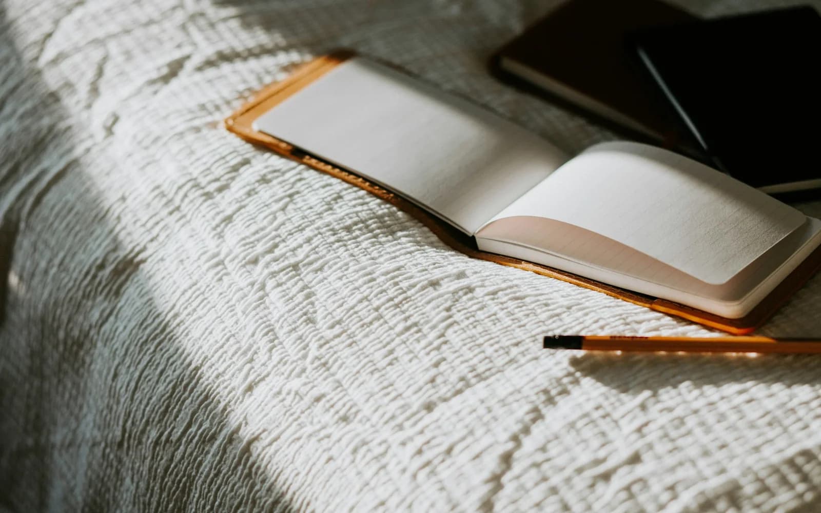 An open notebook and pencil rest on a bedspread.