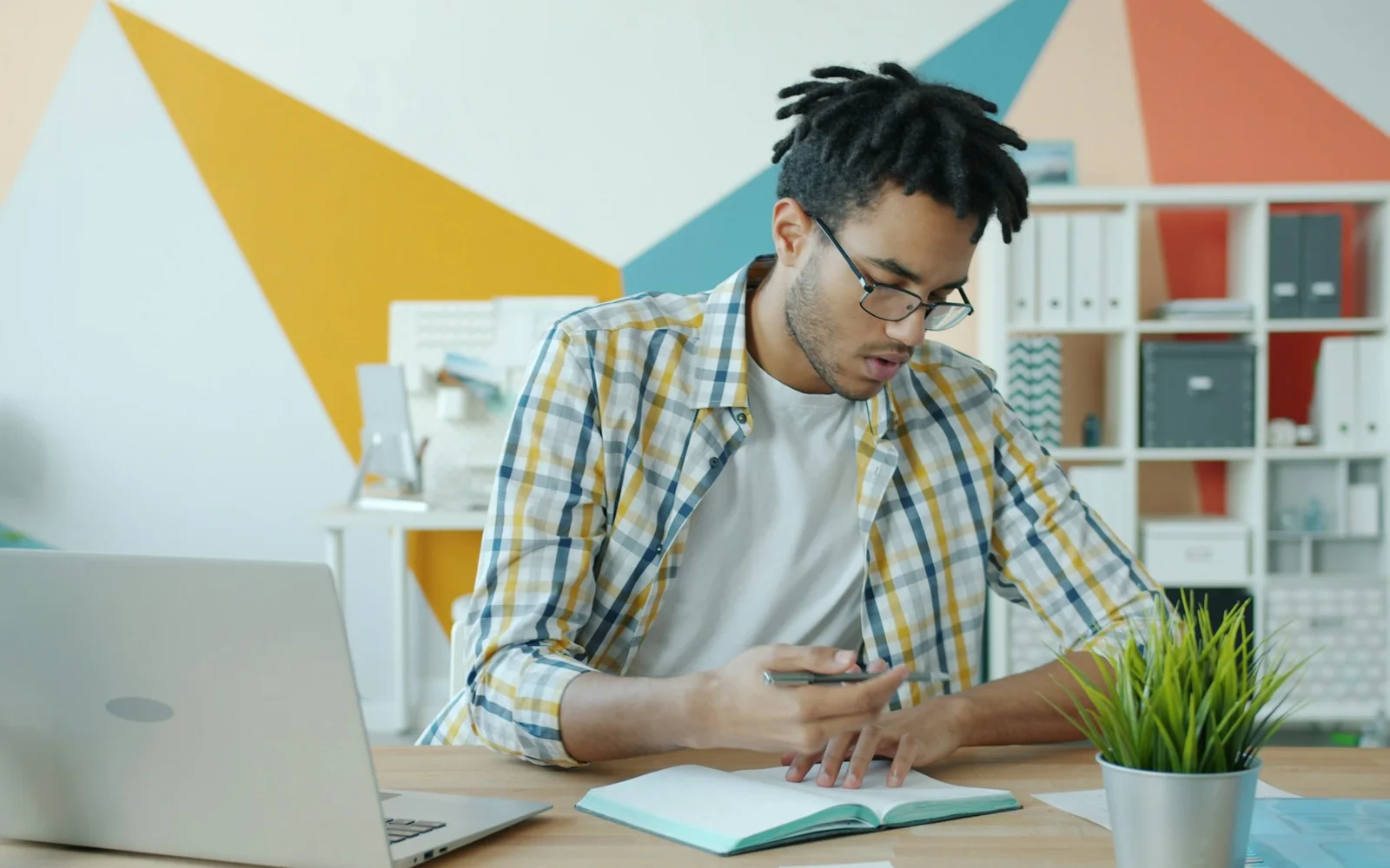 A man writes in a notebook while working beside a laptop.