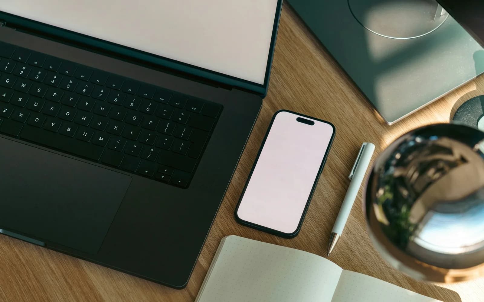 A laptop, phone, and notebook share a wooden desk.