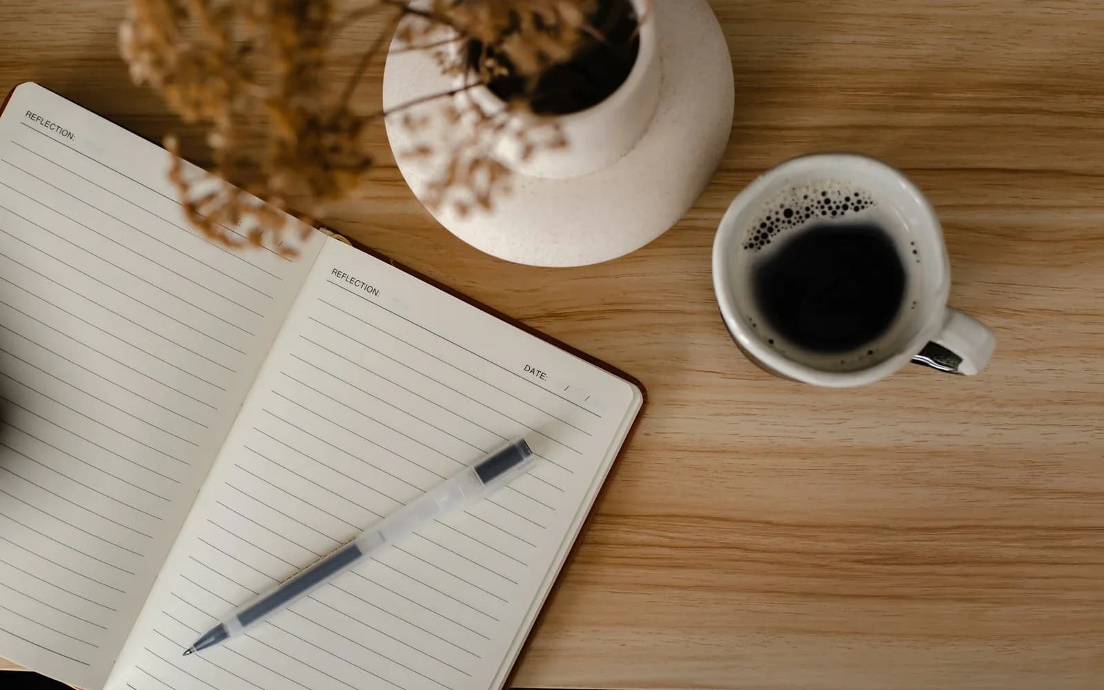 An open notebook and pen sit beside two cups of coffee.