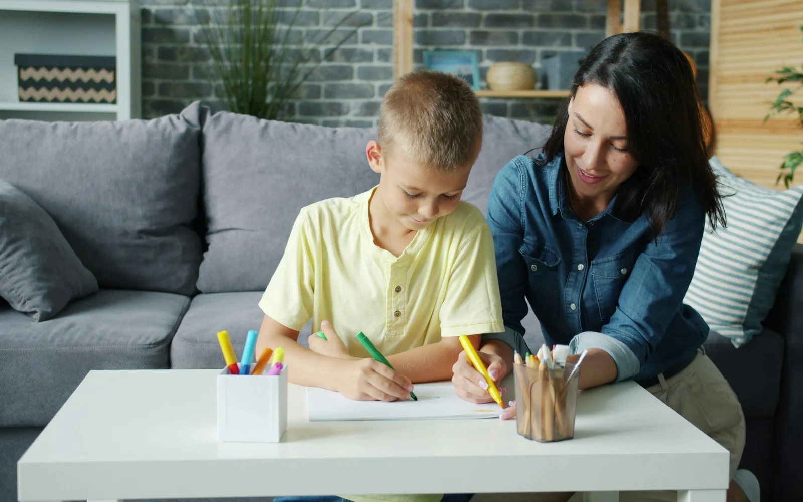 A parent and child draw and write together at a table.
