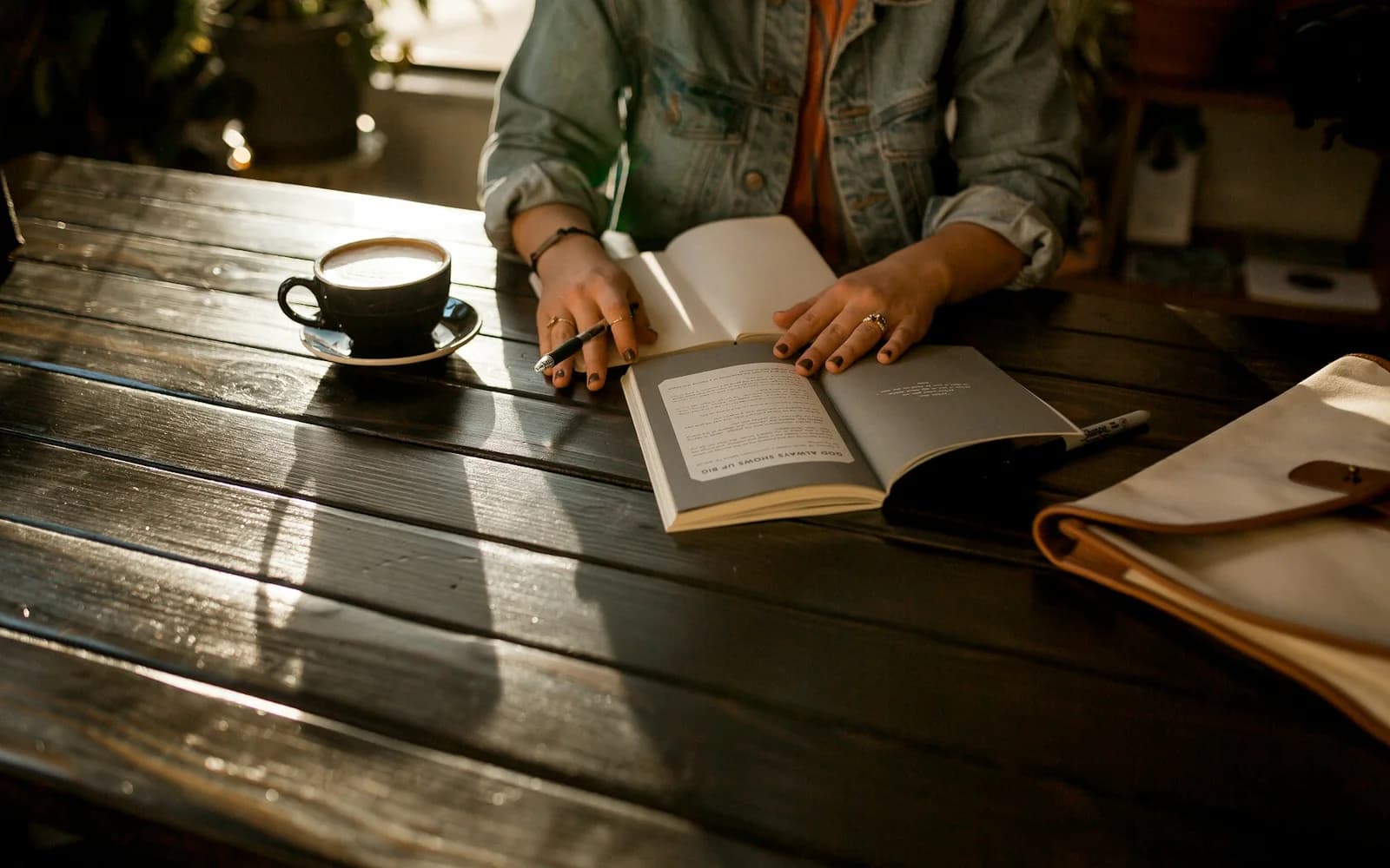 A person opens a notebook beside coffee at a wooden table.