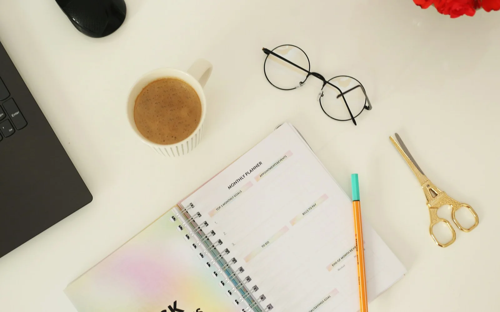 A notebook, pen, glasses, and coffee arranged on a desk.