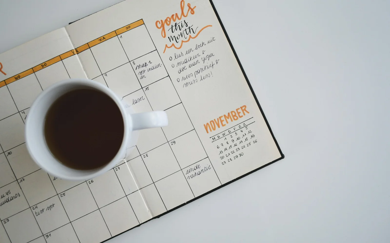 A paper calendar, handwritten notes, and coffee share a desk.