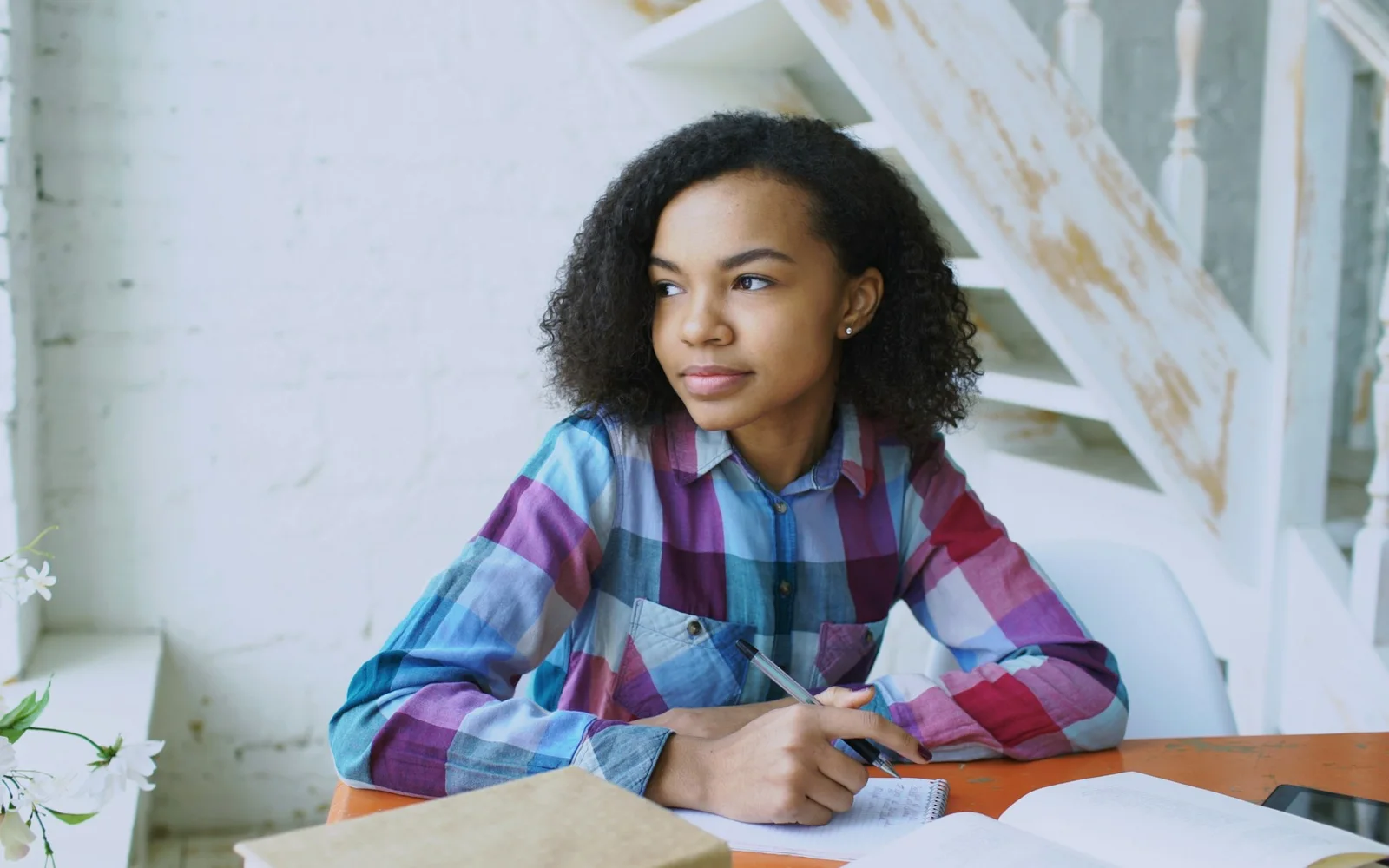 A woman writes in a notebook beside an open laptop.