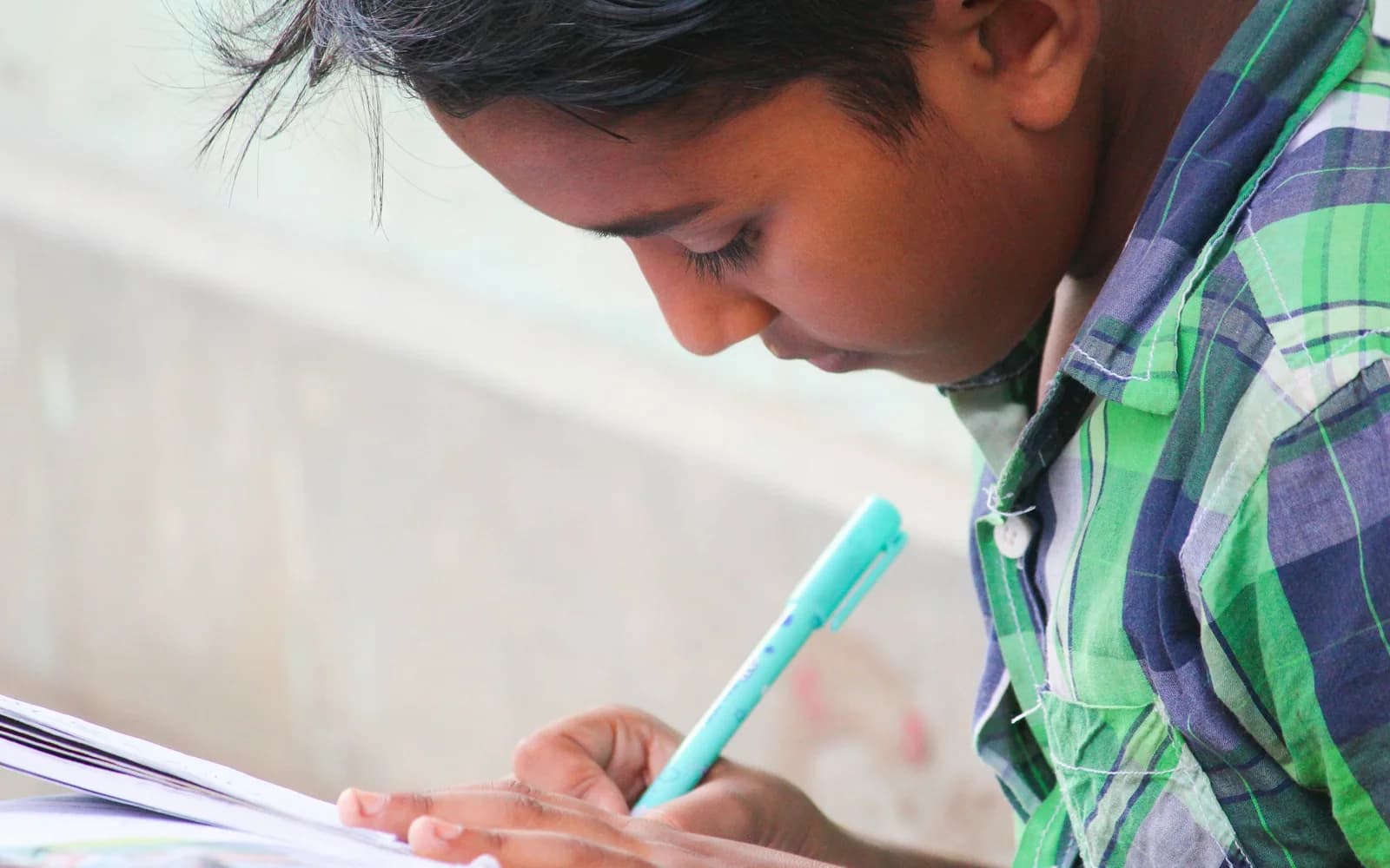 A student writes while using a tablet at a table.