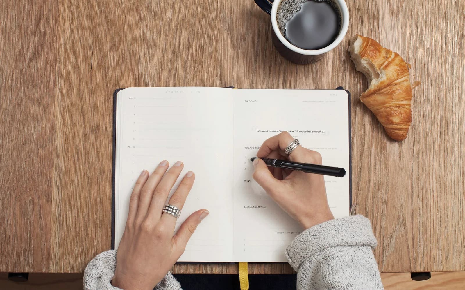 A person starts a notebook entry beside coffee and a croissant.