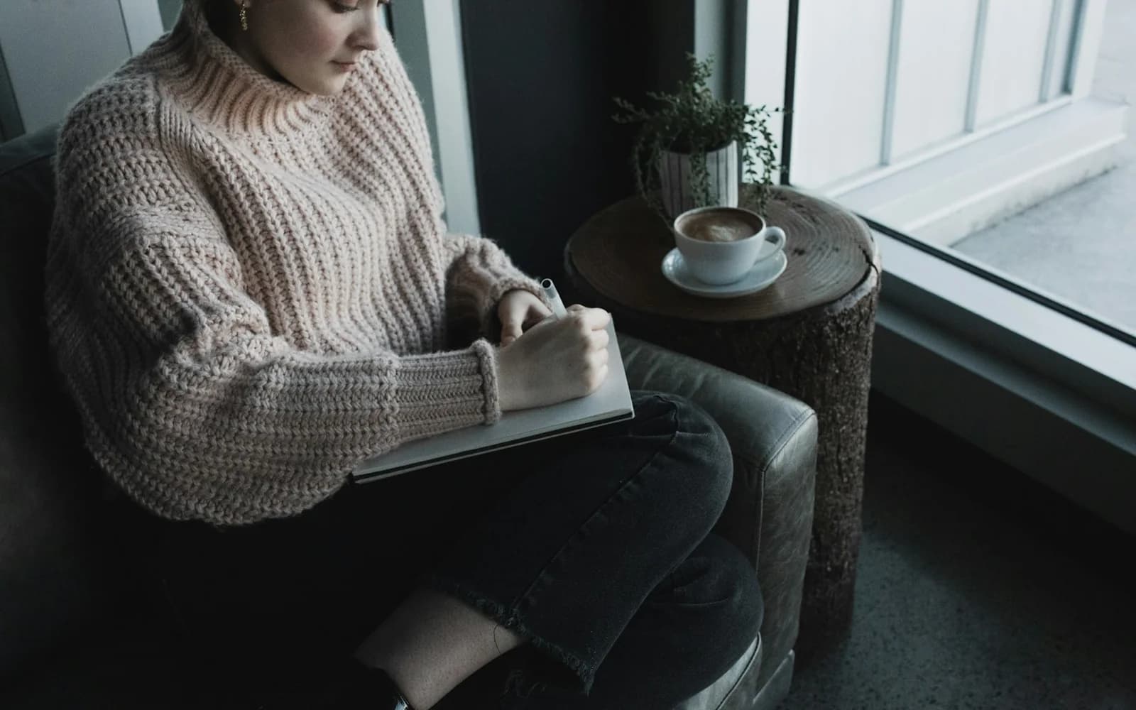 A woman rereads a notebook beside a window and a cup of coffee.