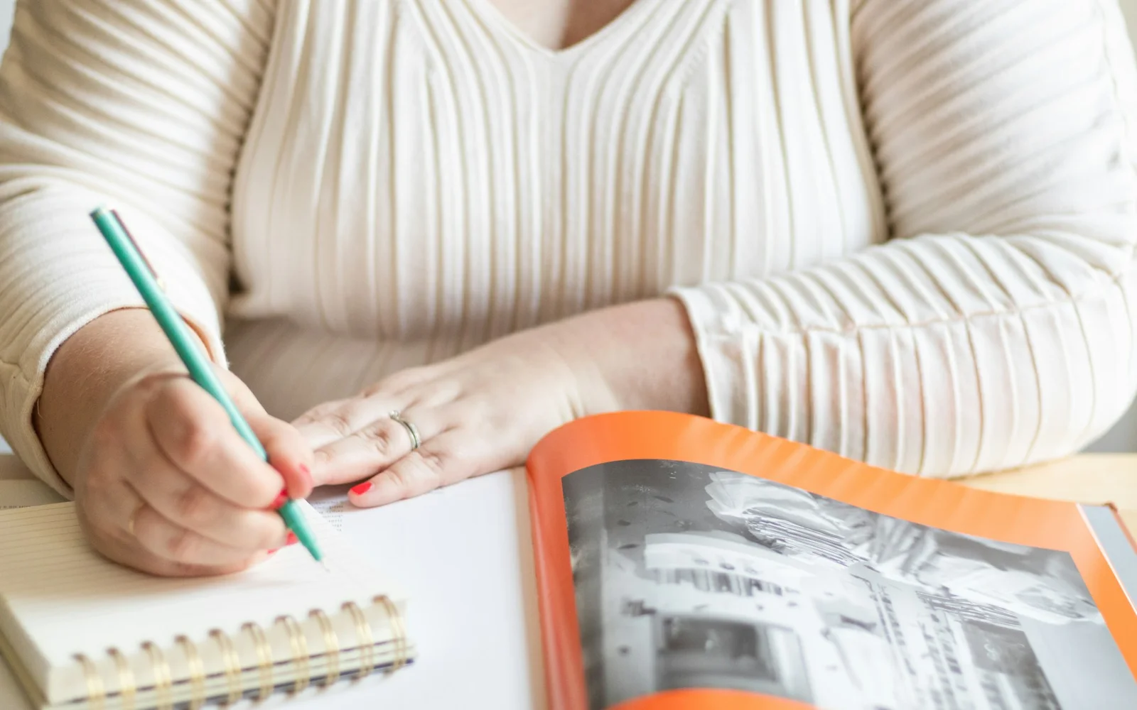 A woman writes in a spiral notebook beside a printed page.