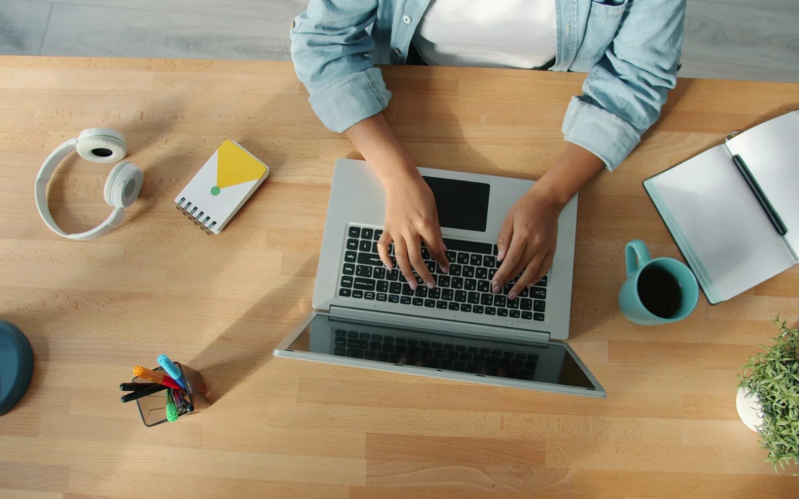 A person types on a laptop beside an open notebook.
