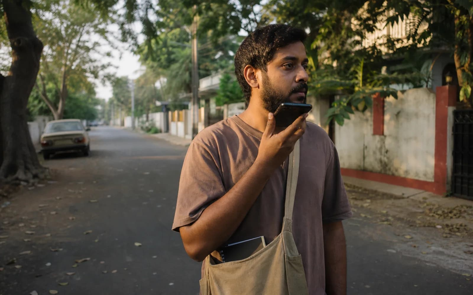 A man records a voice note while carrying a small notebook on a neighborhood walk.